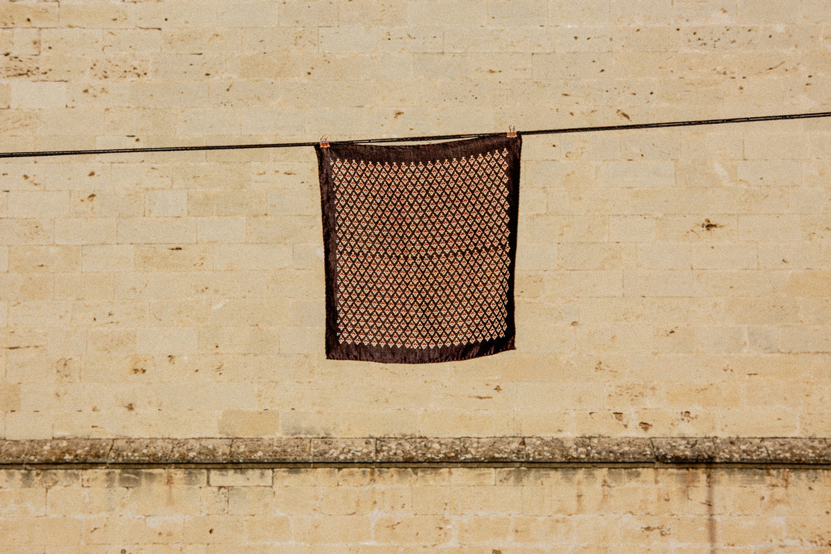 A block-printed silk square pegged on a line against a stone wall