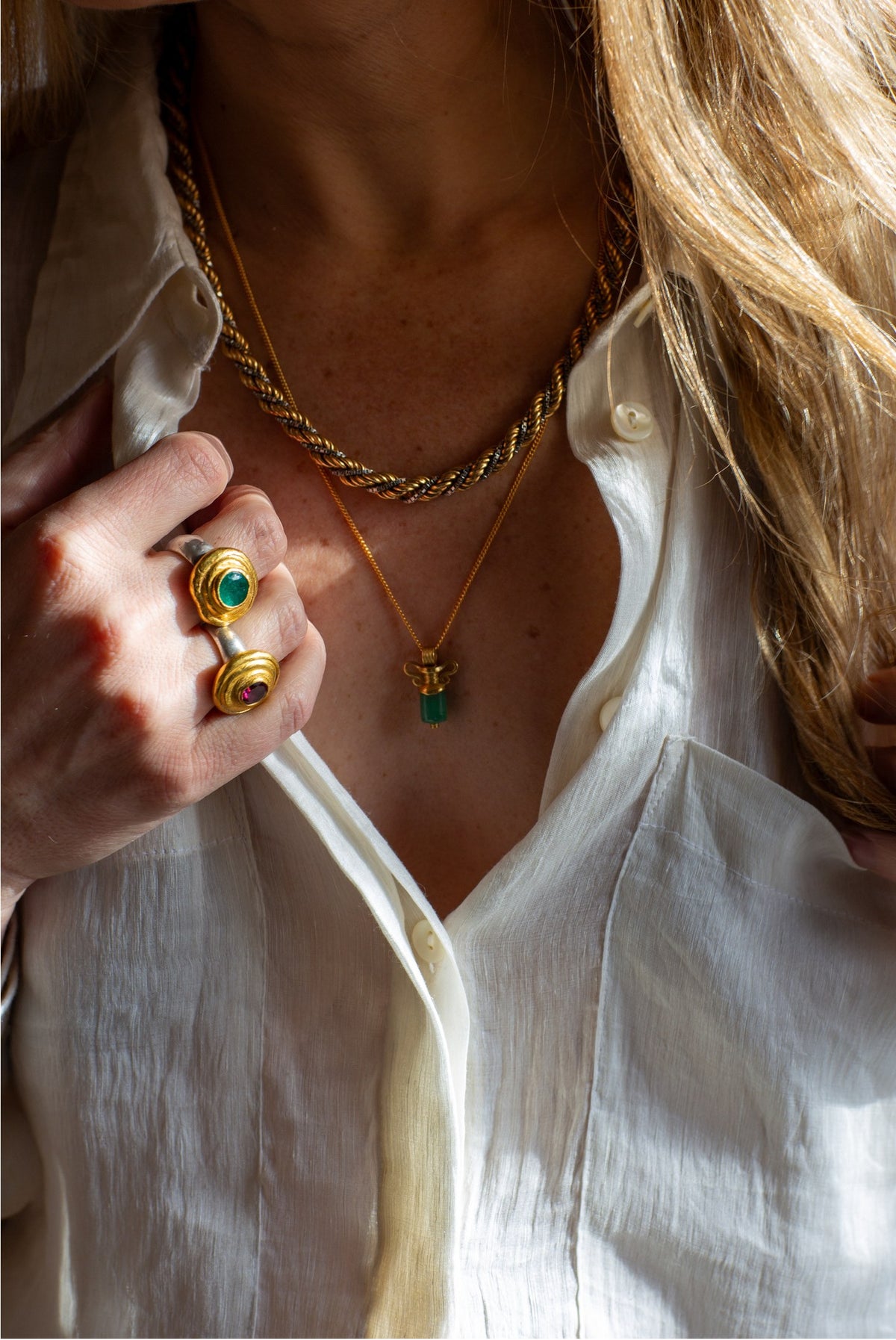 Goldene Ringe und Ketten mit grünen Steinen, getragen zu einem weißen Hemd