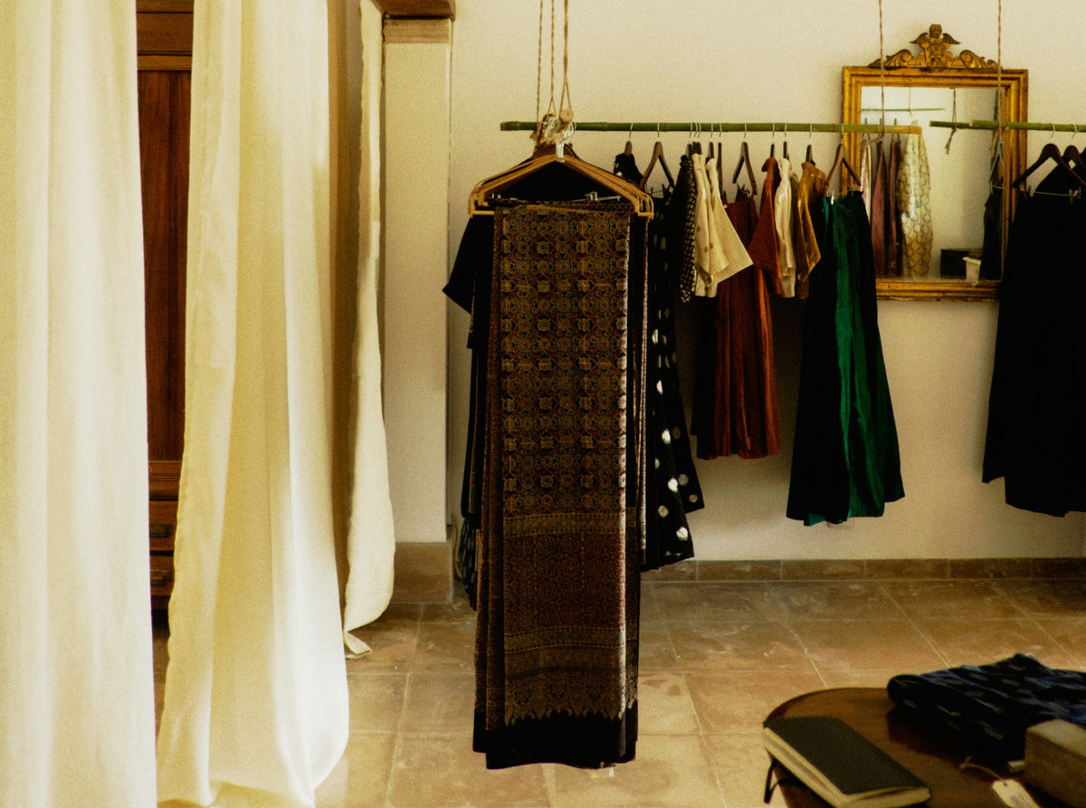 Garments on a wooden rail beside a gilt mirror and a linen curtain