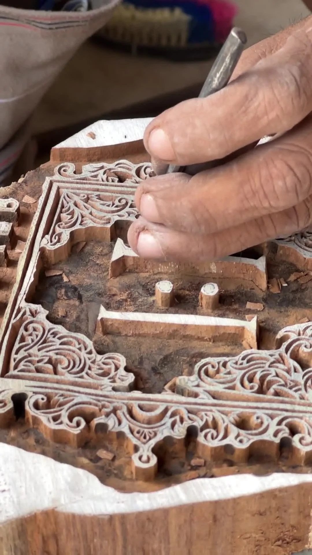 A hand cutting an ornamental pattern into a wooden block