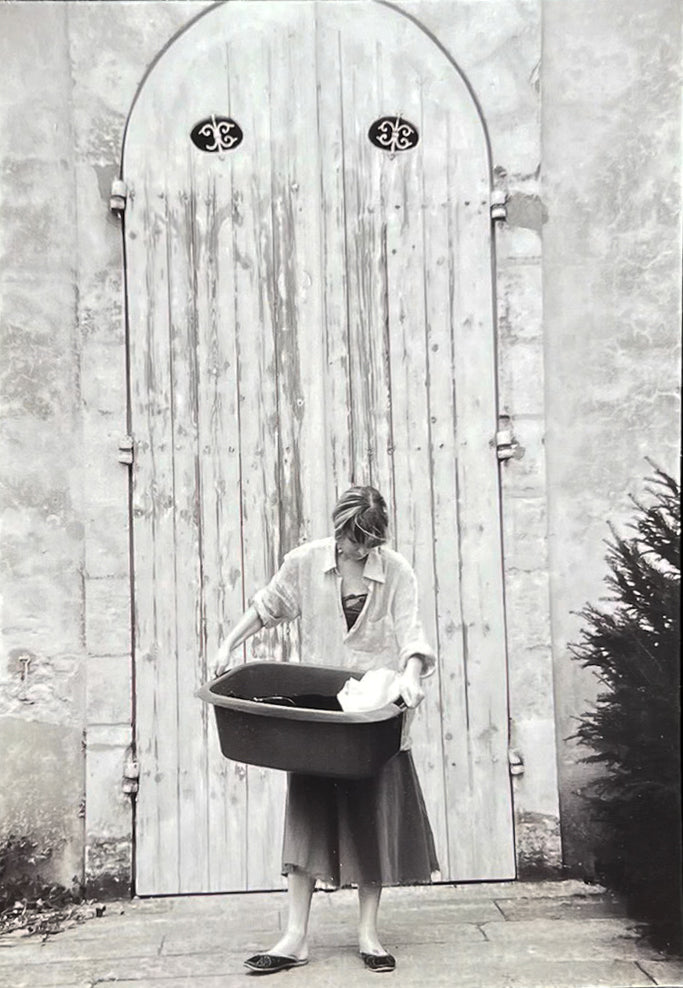 The atelier: a rust shirt and skirt hanging on an open wooden door beside a window and a dressing table